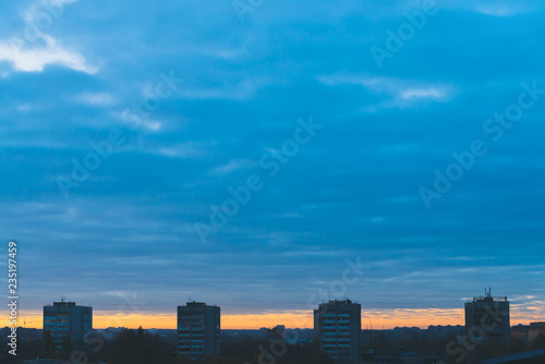 Cityscape with wonderful varicolored vivid dawn. Amazing dramatic blue cloudy sky above dark silhouettes of city buildings. Atmospheric background of orange sunrise in overcast weather. Copy space. © Daniil