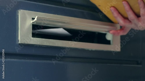 Paper mail being delivered through a door mounted mailbox opening.