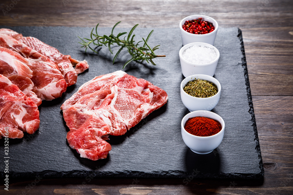 Raw beefsteaks on black stone on wooden background Raw beefsteaks on black stone on wooden background