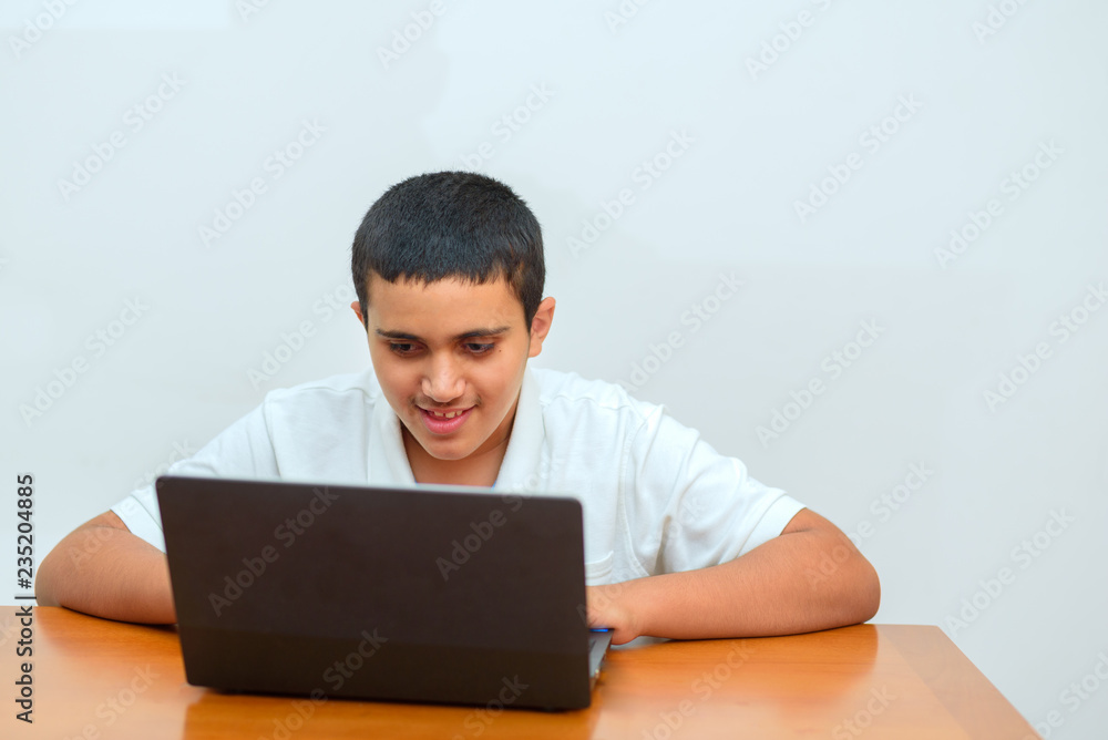 Teenager using new,exciting technology eLearning technology. Kid with laptop sitting at table and studying at home. Black hair boy playing computer games using touchpad. Young businessman using laptop Teenager using new,exciting technology eLearning technology. Kid with laptop sitting at table and studying at home. Black hair boy playing computer games using touchpad. Young businessman using laptop