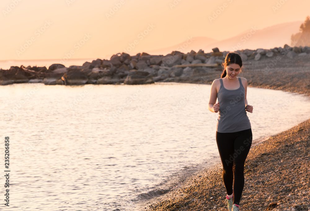 Beautiful young girl run on the beach and smiling. Sunset on the sea at the background. Healthy lifestyle