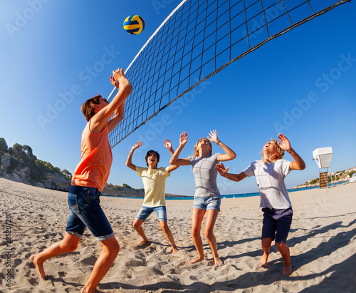 Teenage boy jumping to spike volleyball over net