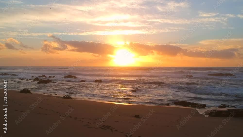Aerial shot flying backwards on beach at sunset looking at setting sun. Silhouetted birds flying Aerial shot flying backwards on beach at sunset looking at setting sun. Silhouetted birds flying