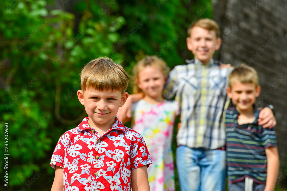 Fototapeta premium Four happy and joyful children, a boy in red clothes is in the foreground, and his friends are behind.