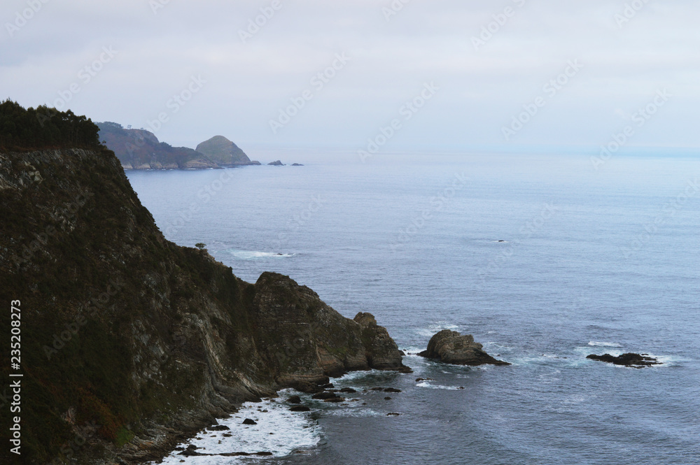 Scenic view of mountains on the horizon and cliffs among sea waves in Cudillero, Spain