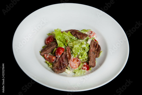 Veal salad, salad with large slices of veal and fresh vegetables on a plate on a black background