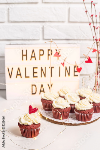 Happy Valentine's Day is written on a decorative lamp next to red cupcakes. Red velvet with mascarpone cream. Valentine's day concept