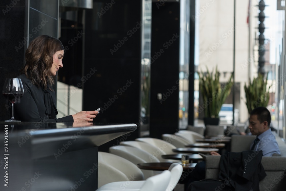 Businesswoman using mobile phone at bar counter while Businesswoman using mobile phone at bar counter while