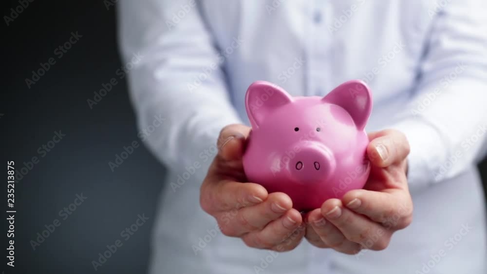 A business woman holds a pink piggy bank in her hands at waist level, copy space on the side. A business woman holds a pink piggy bank in her hands at waist level, copy space on the side.