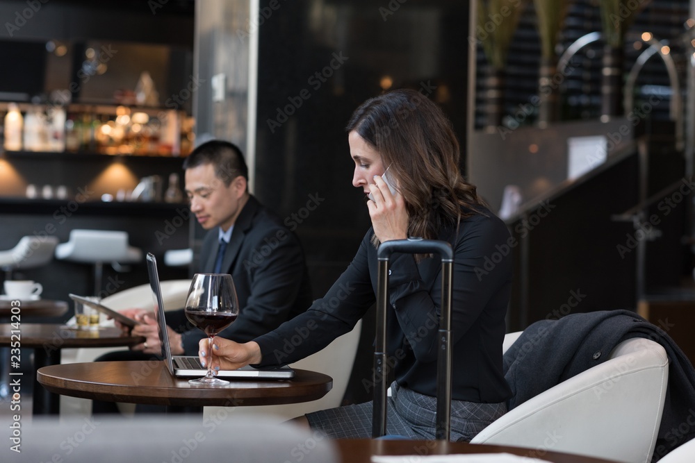 Businesswoman having red wine while talking on mobile phone Businesswoman having red wine while talking on mobile phone
