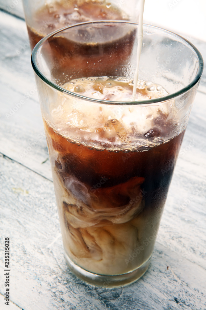 Ice coffee on a rustic table with cream being poured into it showing the texture and refreshing look of the drink Ice coffee on a rustic table with cream being poured into it showing the texture and refreshing look of the drink