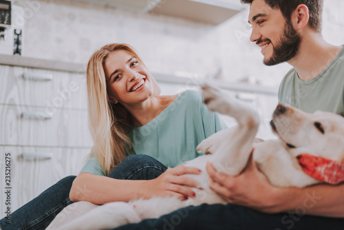 Attractive bearded man and young lady with dog indoors. Woman looking at camera and smiling