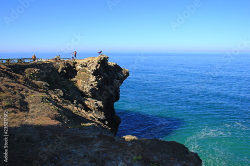 The Atlantic Ocean in Portugal, Penedo da Saudade lighthouse; team of bikers making photosession on the steep rock