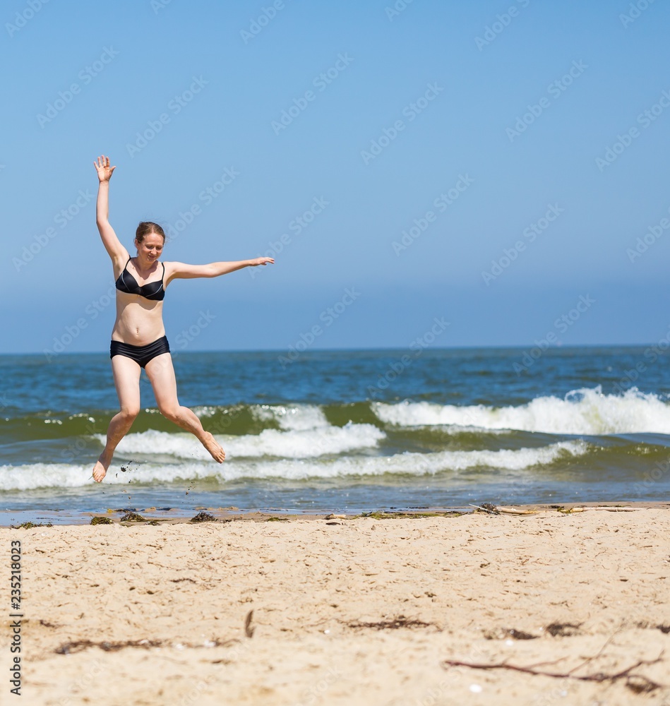 Happy young woman jumping on sea shore at sunny summer day Happy young woman jumping on sea shore at sunny summer day