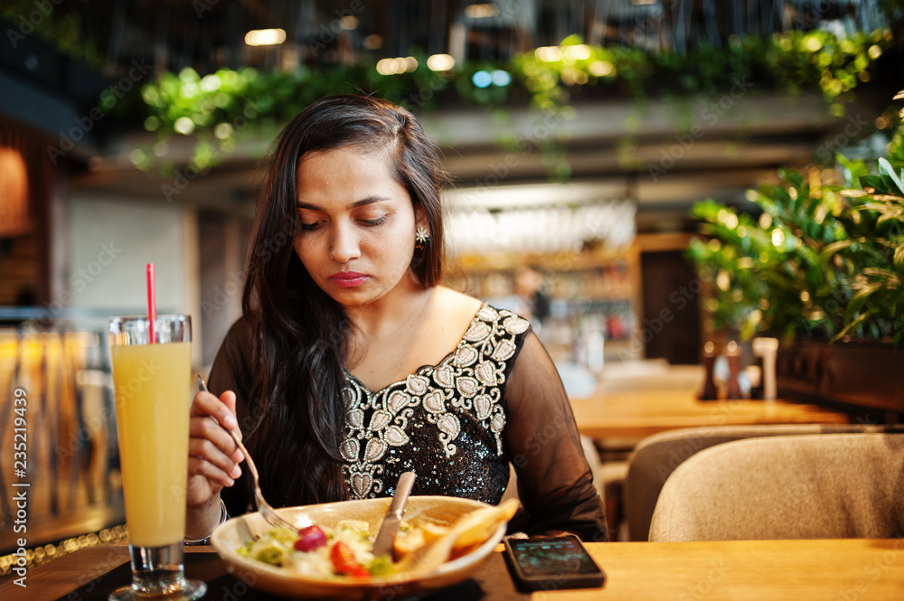 Pretty indian girl in black saree dress posed at restaurant, sitting at table with juice and salad. Pretty indian girl in black saree dress posed at restaurant, sitting at table with juice and salad.