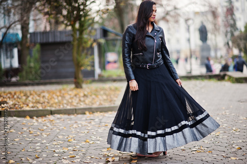 Pretty indian girl in black saree dress and leather jacket posed outdoor at autumn street.