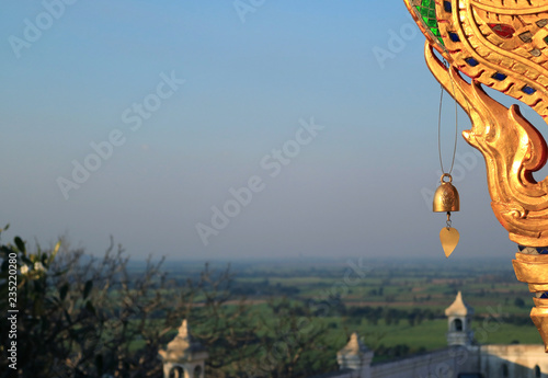 Golden Wind Chime and Decoration of Wat Khao Di Salak Buddhist Temple with Blurred Foothill Landscape in Background, Suphanburi Province, Thailand 