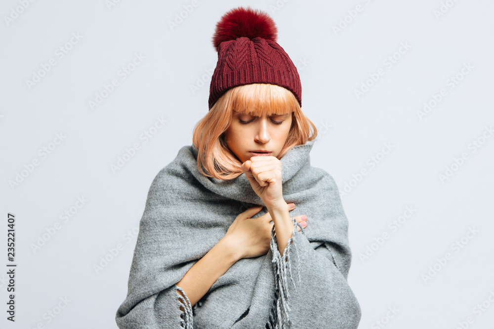 Cute sick young teen woman in red hat, wrapped in warm scarf coughing