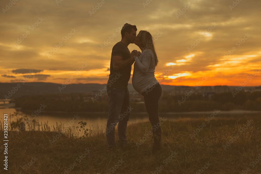 Husband and his pregnant wife kissing while they enjoy spending time together outdoor. Husband and his pregnant wife kissing while they enjoy spending time together outdoor.