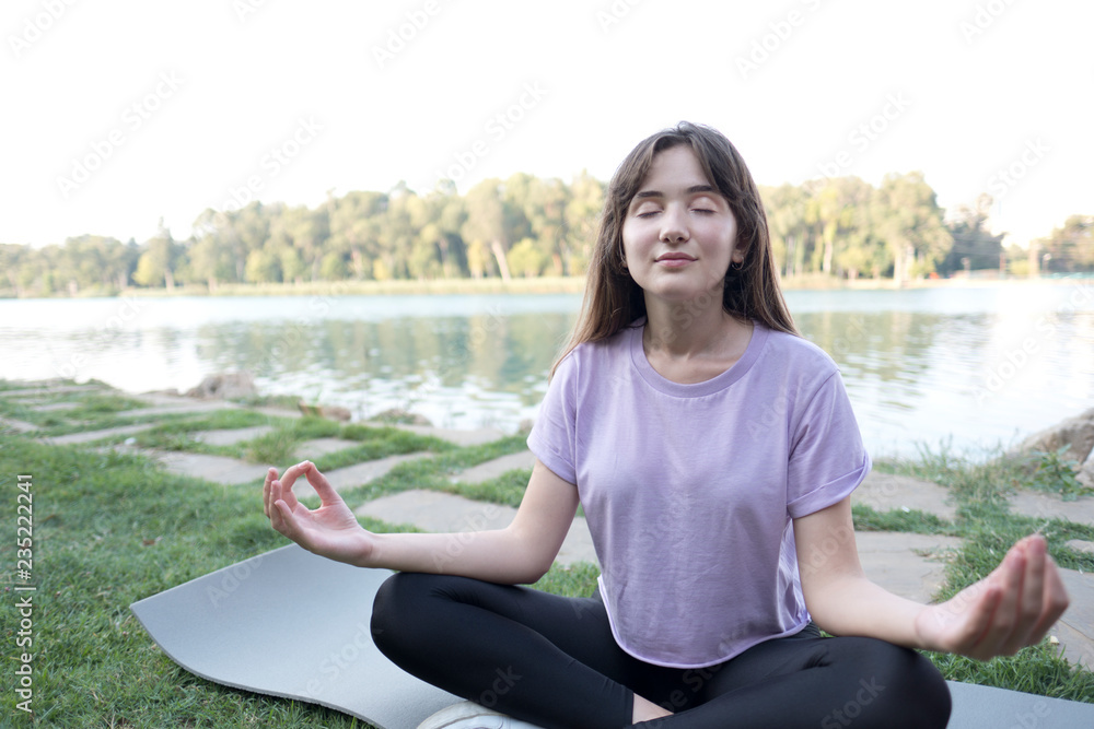 Young beautiful woman doing yoga exercises in park on the bank river.