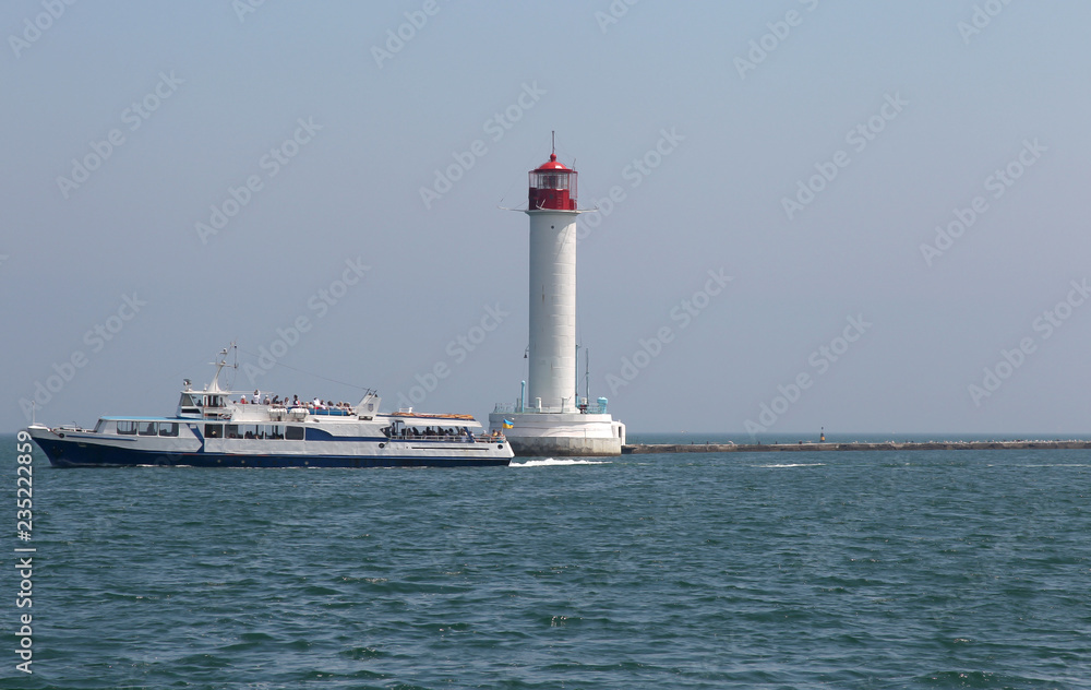 Lighthouse on the sea under the sky. A white sea lighthouse in the middle of the harbor points the path of ships at night and foggy time with light.
