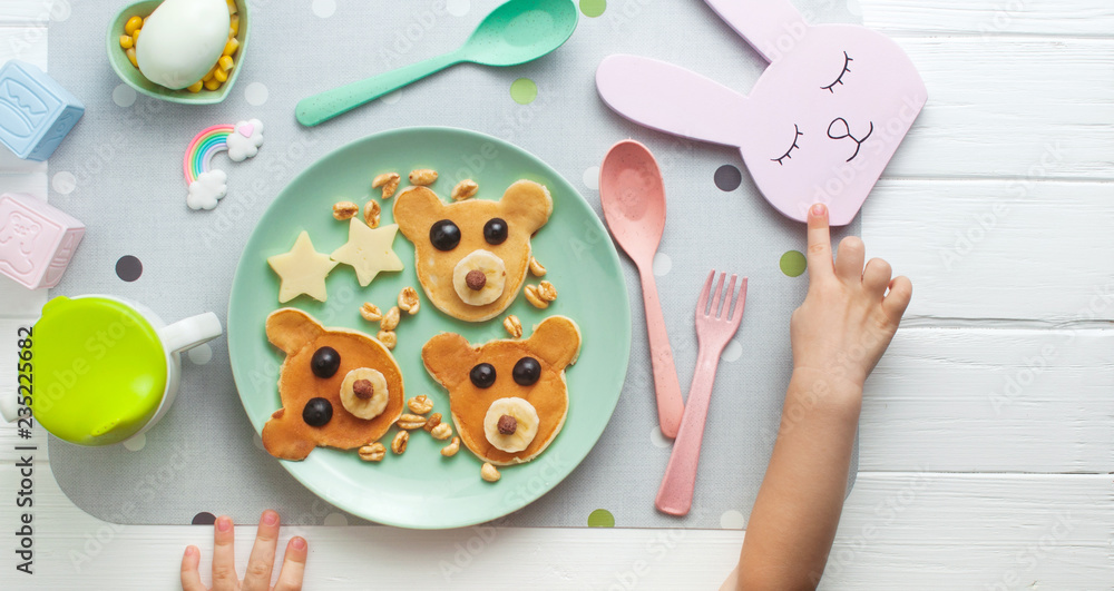 Pink plate with pancakes and kids hands on white wooden background Pink plate with pancakes and kids hands on white wooden background