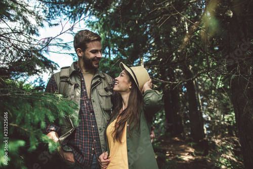 Concept of enjoying journey and adventure in couple. Waist up portrait of happy man and woman looking with love and excitement to each other in sunny green forest