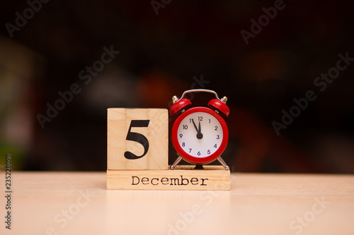 December 5th set on wooden calendar and red alarm clock on dark background.