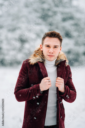 A young man in a coat walking in the snow. Winter day.