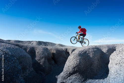 Fotografi Young man riding mountain bike on the background of mountains at blue sky