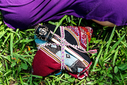 Woman in skirt sitting on green grass in front of maraca and shamanic kit of Quero Peruvian culture