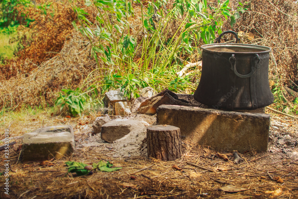 Fototapeta premium Old copper pot for cooking standing on concrete bricks on top of fireplace in the backyard