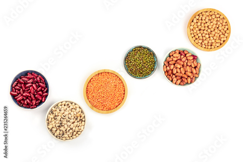 Legumes, shot from the top on a white background with copy space. Red kidney and pinto beans, lentils, chickpeas, soybeans, black eyed peas in bowls with a place for text