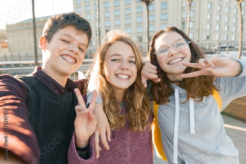 Obraz na płótnie Portrait of three teen friends boy and two girls smiling and taking a selfie outdoors