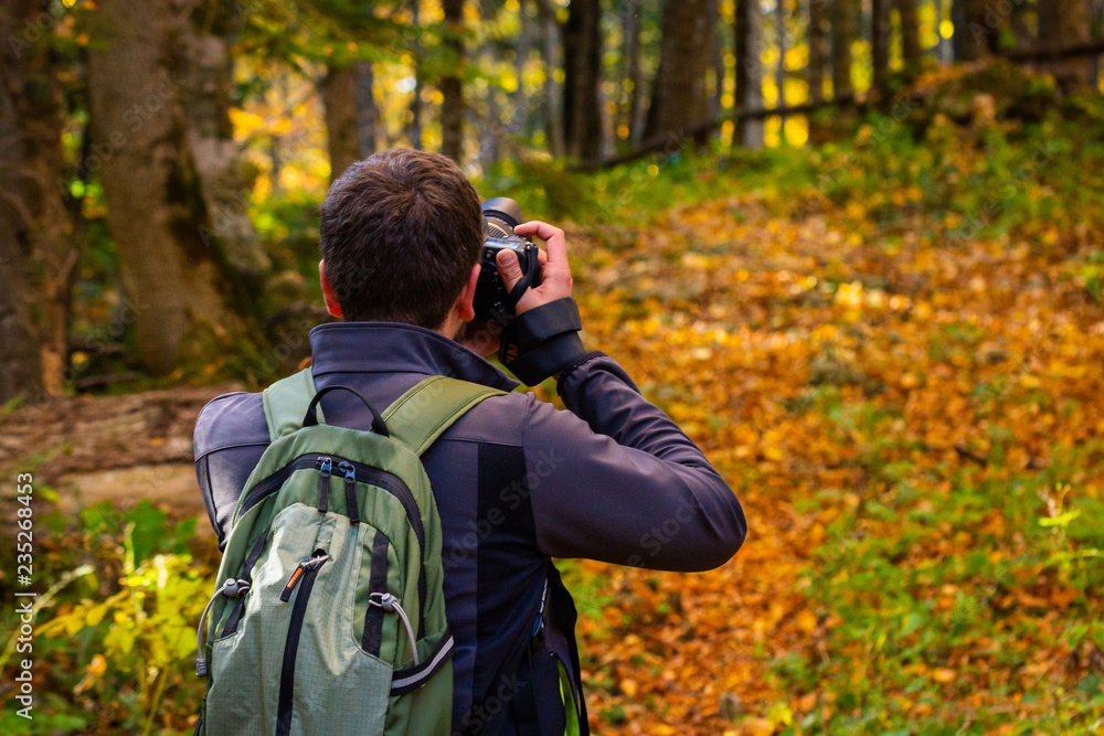 Back view male photographer in bright autumn forest