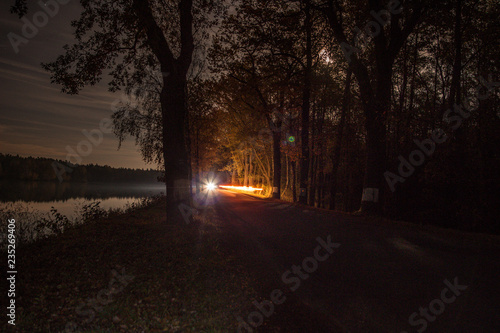 night forest near the pond and car in the distance lights trails
