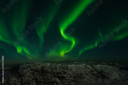 Beautiful stripes of the northern lights, aurora in the night sky above the snow covered hills.