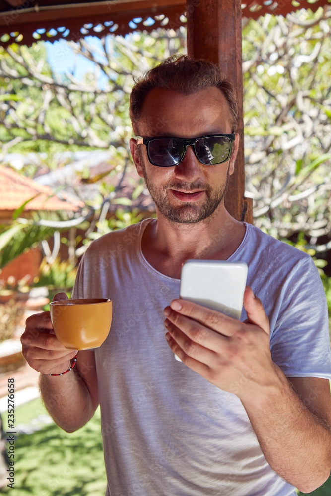 Man using cellphone while drinking coffee / tea on the porch. Man using cellphone while drinking coffee / tea on the porch.