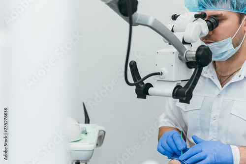 Doctor used microscope. Dentist is treating patient in modern dental office. Operation is carried out using cofferdam. Client is inserted and restored teeth, make denture. Orthodontist and assistant