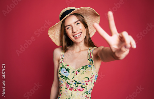Excited and happy beautiful lovely young woman in sunglasses, dress and summer hat is have a fun while posing on pink background