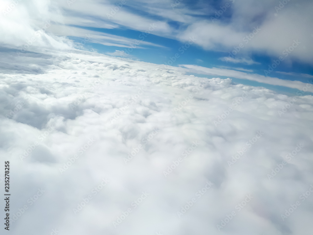 Fototapeta premium A nice aslope view of many clouds from an airplane with a dense and wide base of cumulus clouds in the bottom of the picture, a clear blue sky in the middle and few stratus clouds in the top