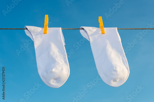 two new, clean, washed,  socks hang on a rope with yellow clothespins.
