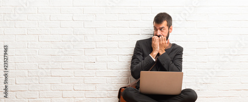 Foto Businessman with his laptop sitting on the floor is a little bit nervous and sca
