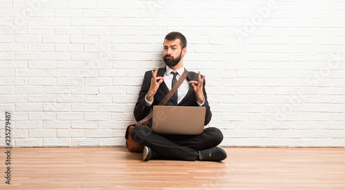 Businessman with his laptop sitting on the floor proud and self-satisfied in love yourself concept