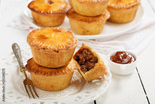 Traditional Australian Mini meat pies from shortbread dough on a white wooden background.