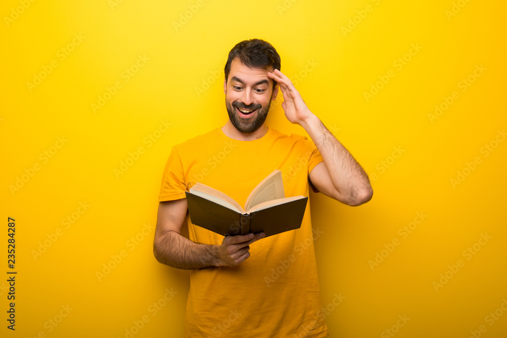 Man on isolated vibrant yellow color holding a book and surprised while enjoying reading Man on isolated vibrant yellow color holding a book and surprised while enjoying reading