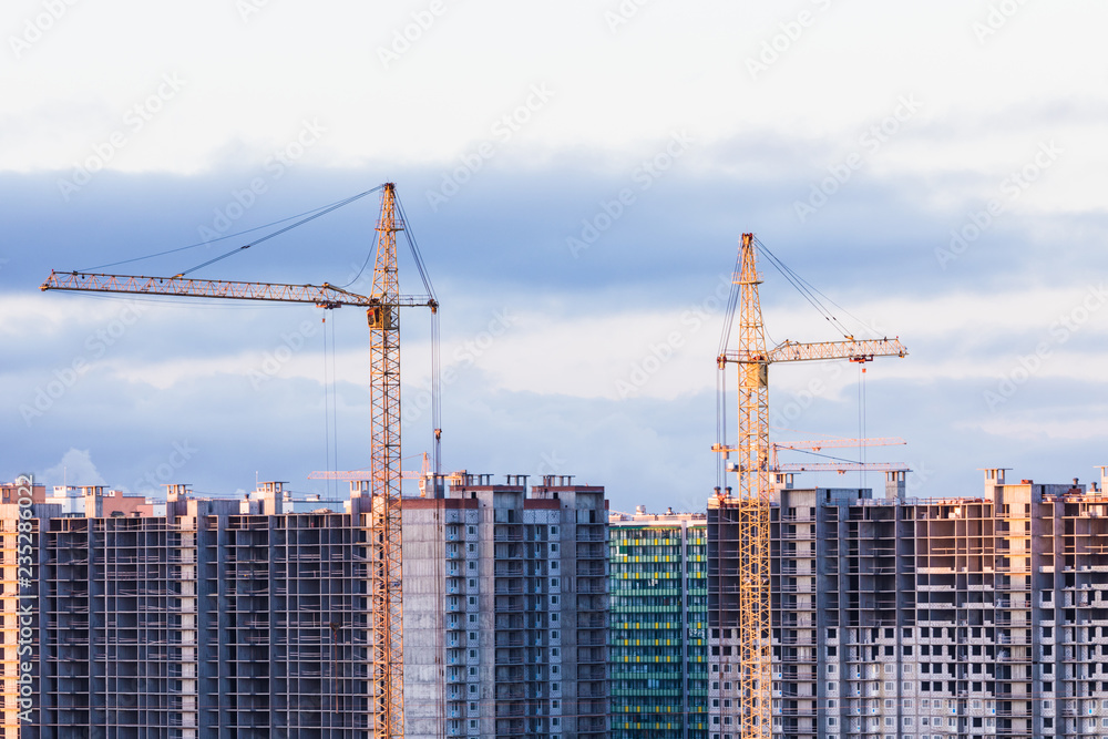 The buildings of new city or town district with the cranes on the background of cloudy sky