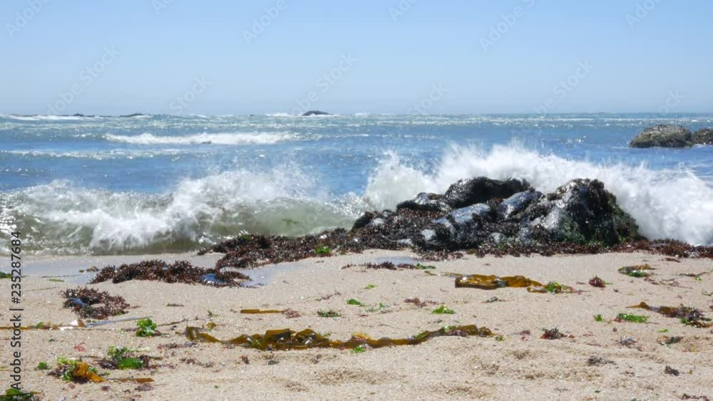 Low angle shot of beach in Portugal as waves crash against rocks on sandy shore and sun glistens on water Low angle shot of beach in Portugal as waves crash against rocks on sandy shore and sun glistens on water