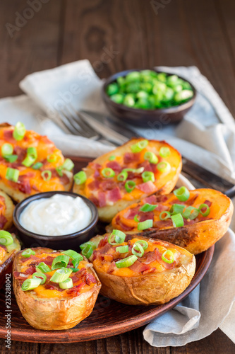 Baked loaded potato skins with cheddar cheese and bacon, garnished with scallions and sour cream vertical