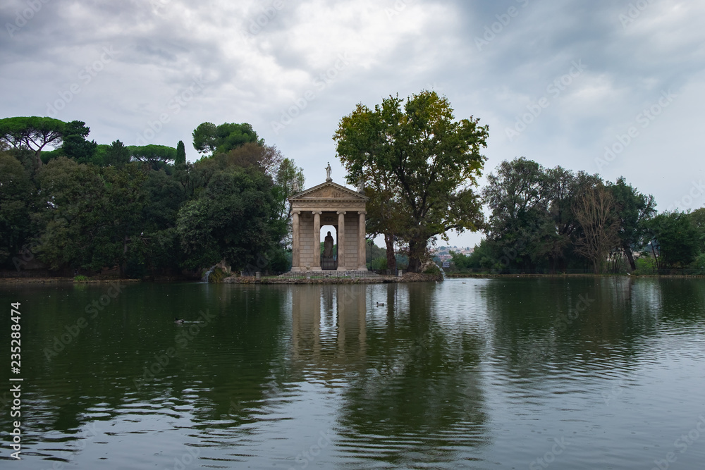 A pond and ancient pavillion with statues in the park of Villa Borghese shot on a rainy October day